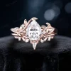 Front view of a 1.25 carat pear-shaped moissanite bypass engagement ring set in 14K rose gold, featuring intricate leaf and vine branch detailing wrapping around the center stone, showcasing the nature-inspired design and brilliant moissanite sparkle.