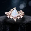 Front view of a 1.25 carat pear cut white opal ring set in 14k rose gold, featuring a nature inspired leaf vine bypass design with an engagement ring and matching wedding band.