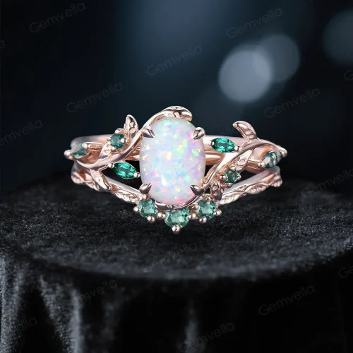 Front view of a nature-inspired bridal ring set featuring a 1.5ct oval white opal center stone, surrounded by emerald and moss agate accents on a 10K rose gold leaf vine branch engagement ring, paired with an emerald wedding band