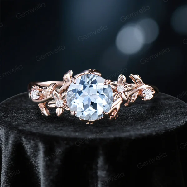 Front view of a vintage style engagement ring featuring a central round cut natural Aquamarine stone surrounded by sparkling moissanite accents, set in 14k yellow gold with an intricate floral leaf and vine branch design.