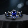 Front view of a black gold ring set featuring a 1.25ct pear cut blue sapphire, showcasing the intricate twig vine gothic design for engagement and wedding.