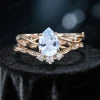 Close-up front view of a 1.25 carat pear cut aquamarine bridal ring set featuring a yellow gold band with detailed moissanite leaf accents, highlighting the center stone's icy blue color and the side stones' brilliance.