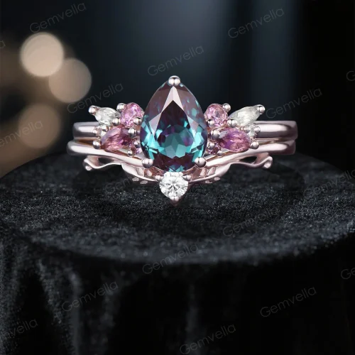 Front - facing view of a 1.25ct pear - shaped alexandrite engagement ring set. The main ring features a cluster of pink tourmaline and moissanite around the pear - cut alexandrite, while the matching band showcases a rose gold branch - leaf design with moissanite accents.