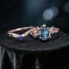 Flat lay display of the handmade bridal set, showing the 1.25ct pear-cut London blue topaz engagement ring and matching blue sapphire wedding band with intricate leaf-branch patterns in rose gold.