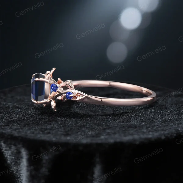 Side profile of the blue sapphire ring, showcasing the intricate leaf and vine design carved into the rose gold band and the height of the gemstone setting.