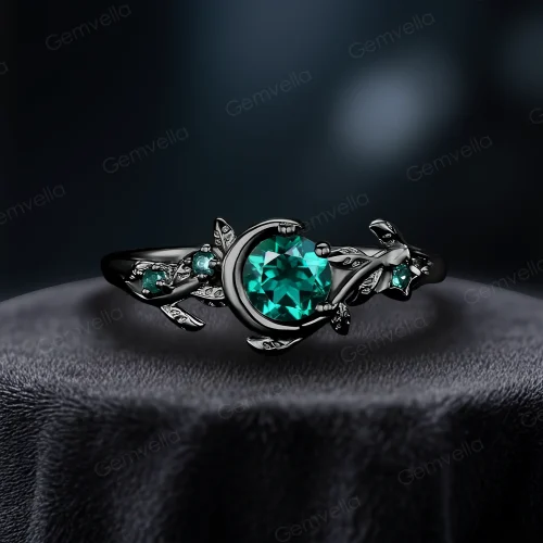 A striking modern black gold engagement ring featuring a 1ct round cut green emerald, combining vintage moon and star elements with a bold, edgy aesthetic.