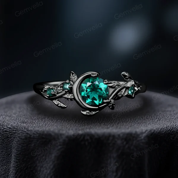 A striking modern black gold engagement ring featuring a 1ct round cut green emerald, combining vintage moon and star elements with a bold, edgy aesthetic.