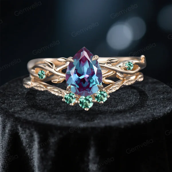 Close-up front view of a 1.25 carat pear cut alexandrite engagement ring set featuring a yellow gold band with detailed green emerald leaf accents and organic twig textures.