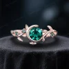 A close-up shot of a 1ct round cut green emerald engagement ring crafted in warm rose gold, featuring a nature-inspired design with dainty leaves and vintage moon and star accents.