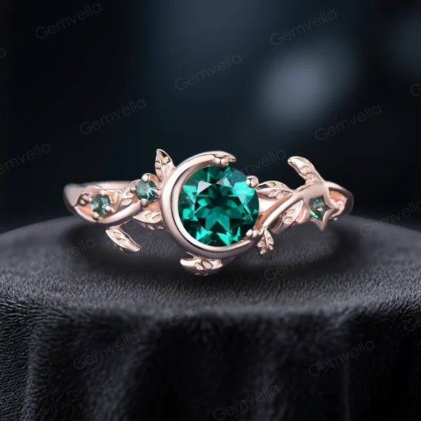 A close-up shot of a 1ct round cut green emerald engagement ring crafted in warm rose gold, featuring a nature-inspired design with dainty leaves and vintage moon and star accents.