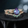 Side profile shot of the 1.25ct pear shaped alexandrite ring on a yellow gold band, highlighting the prong setting height, the curvature of the matching wedding band, and the organic vine texture.