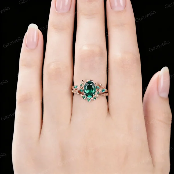 Close up of 1.5ct oval emerald bridal ring set worn on hand, featuring 10K rose gold leaf vine branch design for vintage wedding or anniversary look