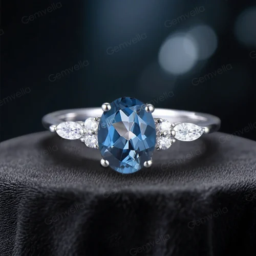 A stunning handmade engagement ring featuring a central 1.5ct oval cut London Blue Topaz flanked by two sparkling marquise cut moissanite stones, set in a delicate band. This unique bridal jewelry piece is perfect as a promise ring or anniversary gift for her.