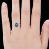 A woman's hand wearing the unique 1.5ct oval London Blue Topaz and marquise moissanite engagement ring. This handmade bridal jewelry makes a beautiful promise ring and anniversary gift for her, showing its elegant scale and sparkle on the finger.