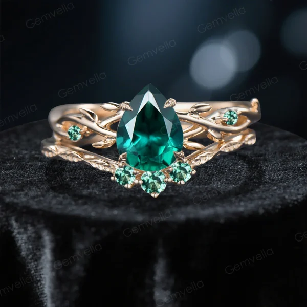 Close-up front view of a 1.25 carat pear cut emerald bridal ring set featuring a nature-inspired yellow gold band with detailed twig and leaf accents surrounding the vivid green center stone.