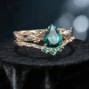 Side profile shot of the 1.25ct pear shaped emerald ring on a yellow gold band, highlighting the prong setting height, the curvature of the matching wedding band, and the organic vine texture.
