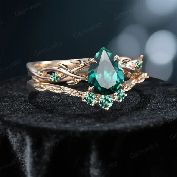 Side profile shot of the 1.25ct pear shaped emerald ring on a yellow gold band, highlighting the prong setting height, the curvature of the matching wedding band, and the organic vine texture.