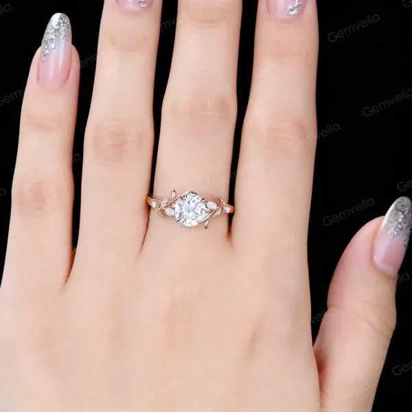 Close up of a woman's hand wearing a vintage rose gold moissanite engagement ring, showcasing the round cut diamond alternative gemstone, leaf vine nature inspired setting and elegant bridal ring fit on finger in real life