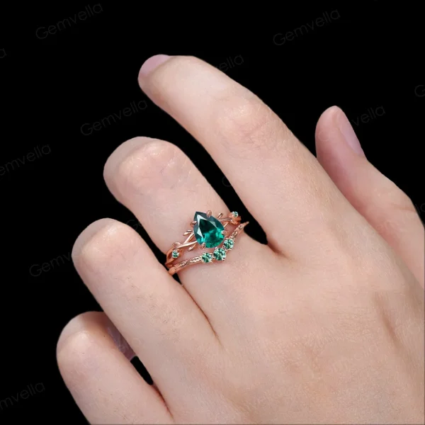 Lifestyle shot of a woman's hand wearing the 1.25ct pear shaped emerald wedding set, showcasing how the nature inspired yellow gold twig ring looks when worn and stacked on the finger.