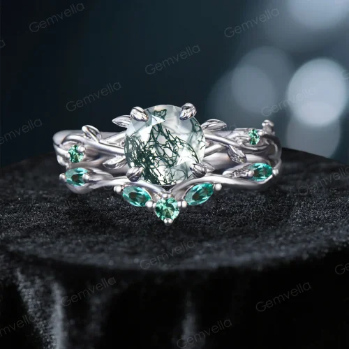 Frontal view of a nature-inspired bridal ring set featuring a unique round cut Moss Agate center stone with organic inclusions, surrounded by an intricate sterling silver twisting vine and leaf setting adorned with vivid green Emerald gems.