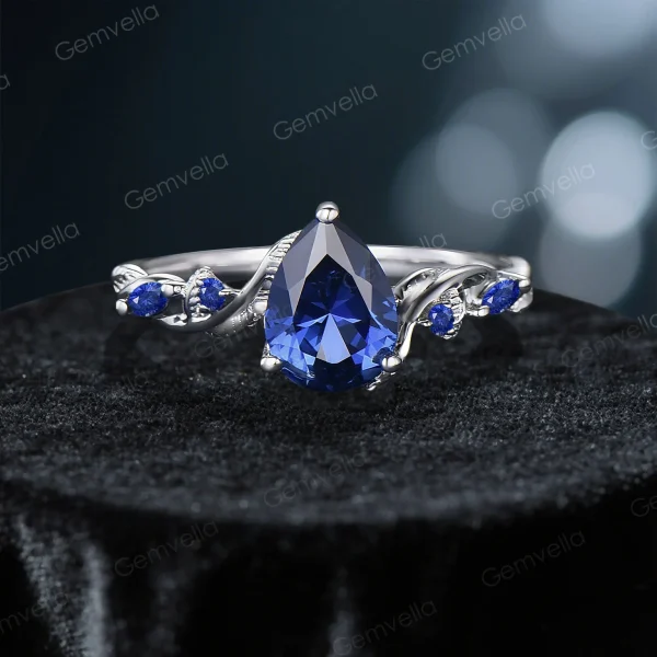 Direct front view of the pear cut blue sapphire center stone in the vintage twig engagement ring, highlighting the symmetrical vine details flanking the stone.
