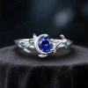 A delicate 925 sterling silver ring featuring a 1ct round blue sapphire stone. The design highlights a vintage moon and star theme with leaf green emerald accents, and subtle leaf engravings on the band for a cohesive nature-inspired aesthetic.