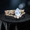 Side profile shot of the 1.25ct pear shaped aquamarine ring on a yellow gold band, highlighting the prong setting height, the curvature of the matching wedding band with sparkling moissanite leaves, and the organic vine texture.