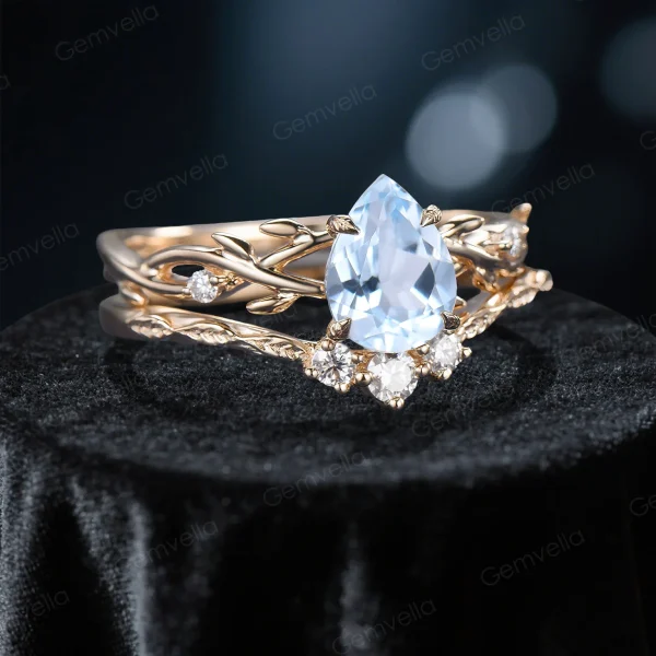 Side profile shot of the 1.25ct pear shaped aquamarine ring on a yellow gold band, highlighting the prong setting height, the curvature of the matching wedding band with sparkling moissanite leaves, and the organic vine texture.