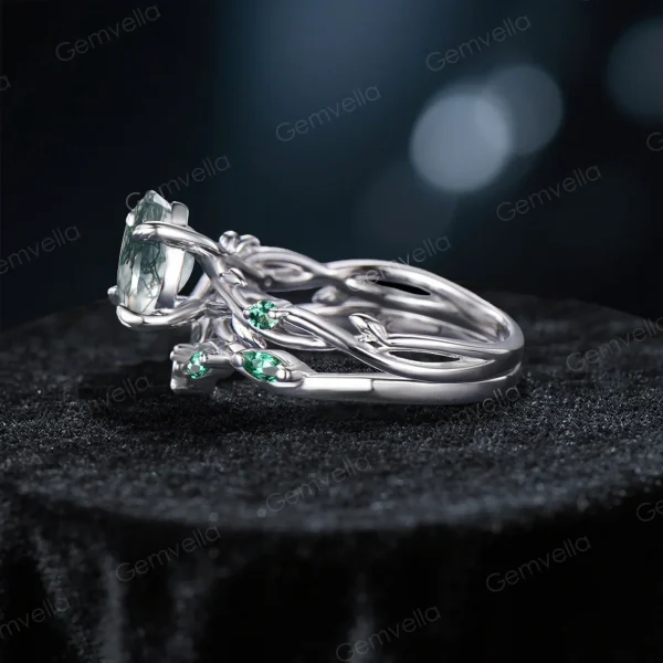 Side profile showcasing the substantial width of the sterling silver band, the raised cathedral setting of the Moss Agate, and the detailed leaf texture wrapping around the side of the ring shank with embedded Emerald stones.