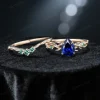 Flat lay photography of the nature inspired blue sapphire engagement ring and wedding band set separated to show the intricate emerald leaf details and the pear shaped blue gemstone.