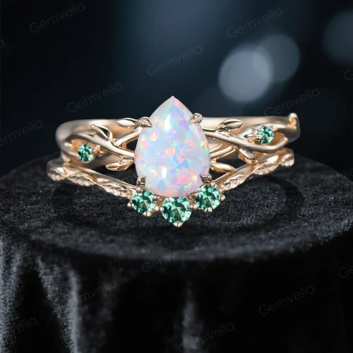 Close-up front view of a 1.25 carat pear cut opal bridal ring set featuring a yellow gold band with detailed green emerald leaf accents, highlighting the gemstone's vibrant play-of-color.