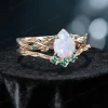 Side profile shot of the 1.25ct pear shaped opal ring on a yellow gold band, highlighting the prong setting height, the curvature of the matching wedding band, and the organic vine texture with emerald leaves.