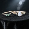 Flat lay photography of the nature inspired opal engagement ring and wedding band set separated to show the intricate emerald leaf details and the pear shaped center stone's fire.