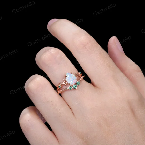 Lifestyle shot of a woman's hand wearing the 1.25ct pear shaped opal wedding set, showcasing how the nature inspired yellow gold twig ring with emerald leaves looks when worn and stacked on the finger.