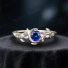 Close-up of a vintage style blue sapphire ring crafted in solid 14k yellow gold. The round cut blue sapphire is accented by genuine green emeralds in a celestial moon and star setting, with leaf motifs etched into the band for a nature-inspired look.