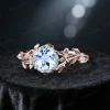 Angled perspective of a nature inspired engagement ring showcasing the round natural Aquamarine center stone and halo of moissanite accents, revealing the 14k gold floral leaf vine branch details on the shank.