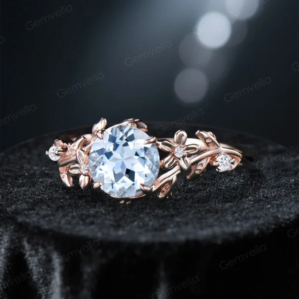 Angled perspective of a nature inspired engagement ring showcasing the round natural Aquamarine center stone and halo of moissanite accents, revealing the 14k gold floral leaf vine branch details on the shank.