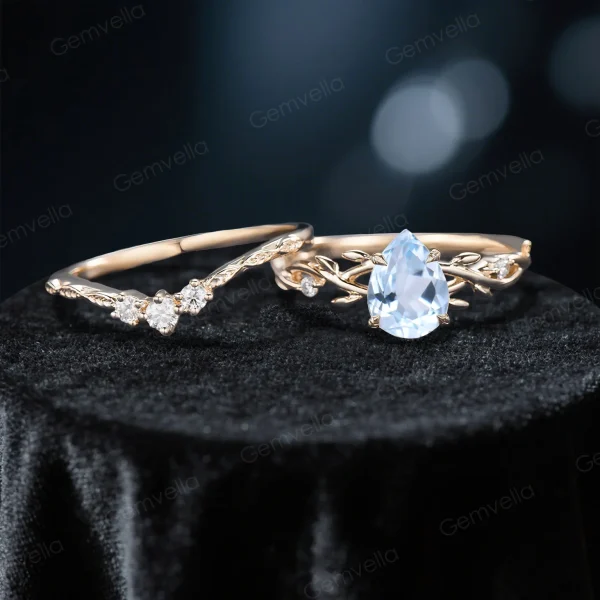 Flat lay photography of the nature inspired aquamarine engagement ring and wedding band set separated to show the intricate moissanite leaf details and the pear shaped pale blue gemstone.