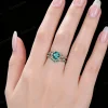 Lifestyle close-up of a woman's hand wearing the vintage 1.2ct round cut green emerald ring, demonstrating the dainty stackable vine leaf design on the finger.