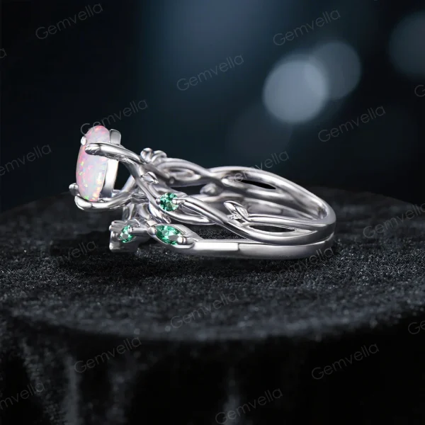 Side profile showing the twisting vine leaf band with green emerald accents and the opal center stone setting.
