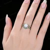 Lifestyle close-up of a woman wearing the vintage opal engagement ring set with green emerald accents, showing the dainty stackable vine leaf design on finger.