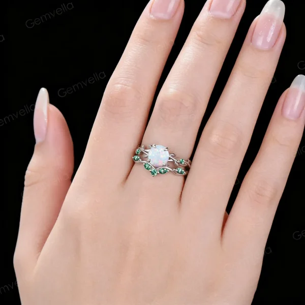 Lifestyle close-up of a woman wearing the vintage opal engagement ring set with green emerald accents, showing the dainty stackable vine leaf design on finger.