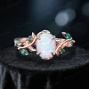 Front view of the nature-inspired engagement ring alone, showcasing the 1.5ct oval white opal center stone, 10K rose gold leaf vine branch band, and emerald and moss agate accent stones set along the sides