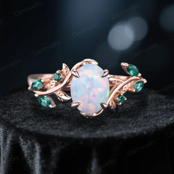 Front view of main ring from 1.5ct oval cut white opal and emerald bridal set, featuring the nature inspired 10K rose gold leaf vine branch design with central opal and emerald accents