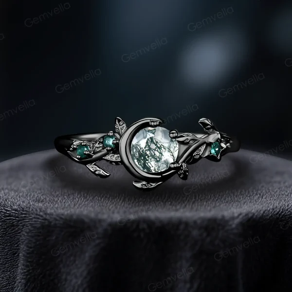 A striking side view of a 1ct round cut natural moss agate ring set in black gold. The vintage moon and star design features contrasting green emerald accents, creating a unique and modern nature-inspired look for women.