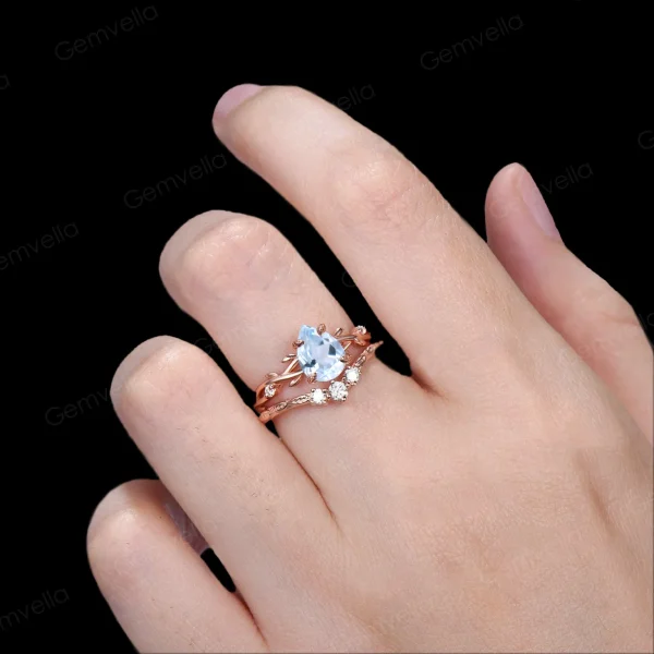Lifestyle shot of a woman's hand wearing the 1.25ct pear shaped aquamarine wedding set, showcasing how the nature inspired yellow gold twig ring with sparkling moissanite leaves looks when worn and stacked on the finger.