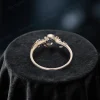 Top down view showing the band width and thickness of the blue sapphire engagement ring. The image details the sturdy vintage setting, the round cut sapphire center, the placement of green emerald accents on the moon star design, and leaf engravings along the band.