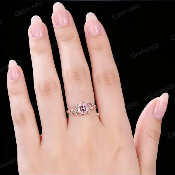 Close up of a woman's hand wearing a vintage round cut pink sapphire engagement ring with pink tourmaline accents and 14k gold floral leaf vine branch design showing how it looks when worn