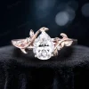 Close-up front view of the main 1.25 carat pear-shaped moissanite center stone in a bypass setting, surrounded by delicate 14K rose gold leaf and vine branch accents, showcasing the brilliant cut and nature-inspired engagement ring design.