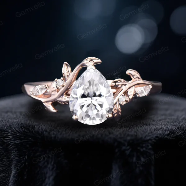 Close-up front view of the main 1.25 carat pear-shaped moissanite center stone in a bypass setting, surrounded by delicate 14K rose gold leaf and vine branch accents, showcasing the brilliant cut and nature-inspired engagement ring design.